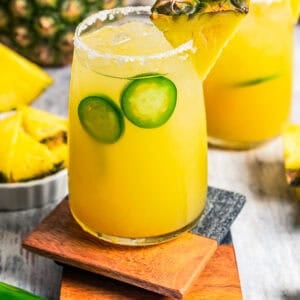 Pineapple margaritas served in drinking glasses with a garnish of jalapeno slices and pineapple wedges.