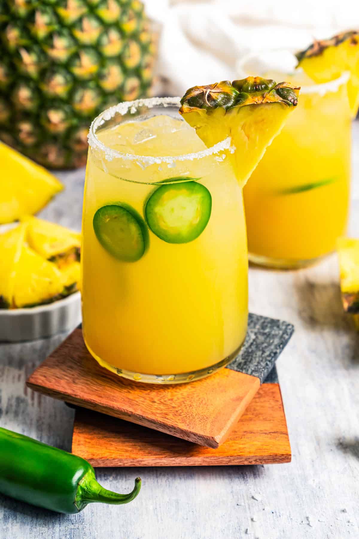 This easy pineapple margarita is a juicy blend of tequila blanco, fresh pineapple juice, and lime, shaken over ice. Don’t forget a salt rim! Pineapple margaritas served in drinking glasses with a garnish of jalapeno slices and pineapple wedges.