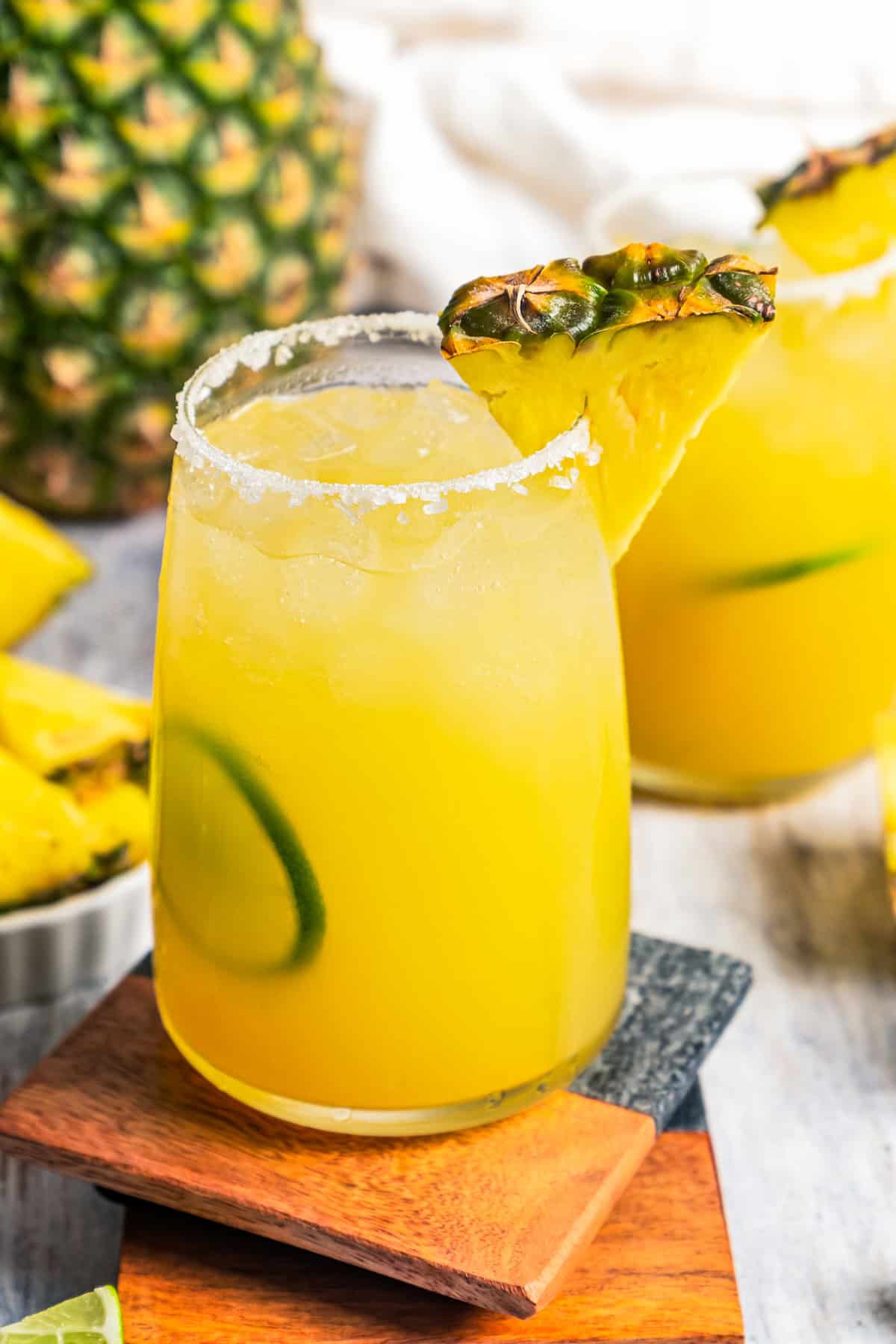 This easy pineapple margarita is a juicy blend of tequila blanco, fresh pineapple juice, and lime, shaken over ice. Don’t forget a salt rim! Pineapple margaritas served in drinking glasses.