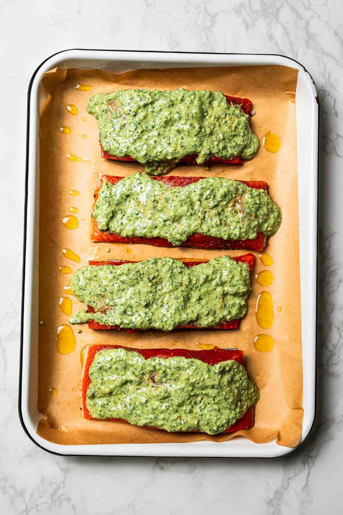 Salmon filets topped with creamy zhoug sauce on a parchment-lined baking sheet.