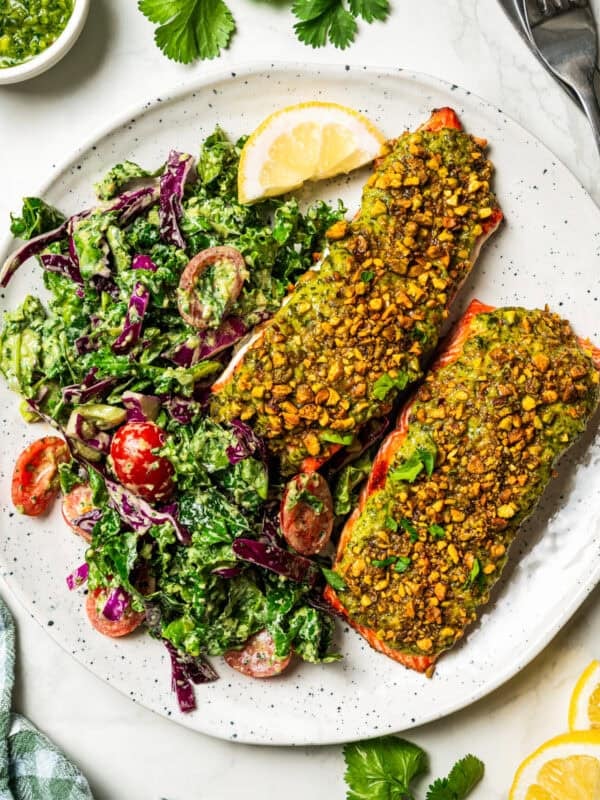 Two pistachio crusted salmon filets with a side of kale salad on a plate.