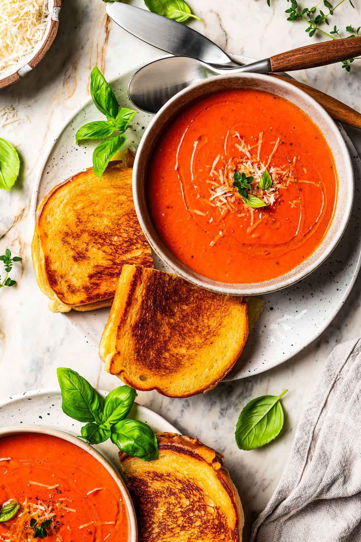 Overhead view of a bowl of tomato soup next to a grilled cheese on a plate.