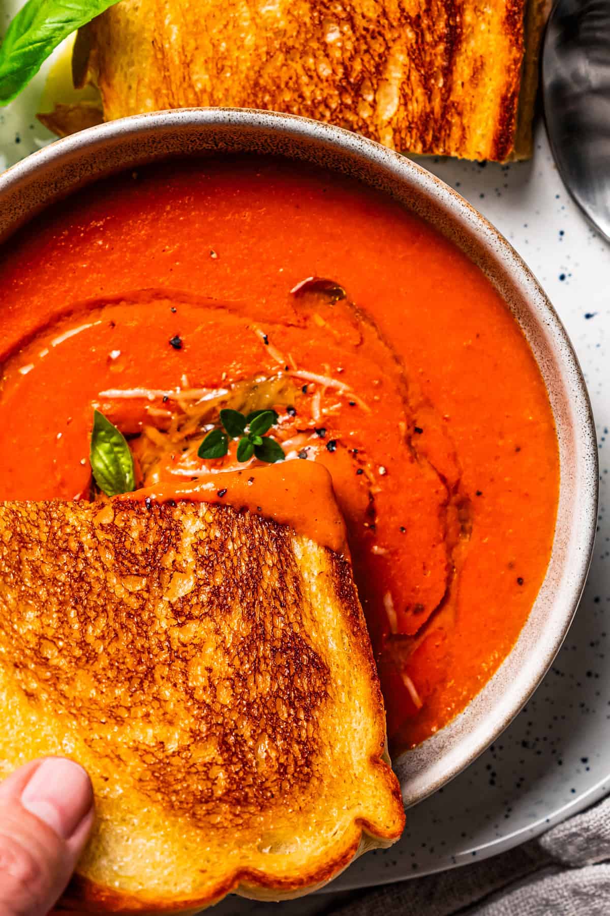 A hand dipping a grilled cheese sandwich into a bowl of tomato soup.