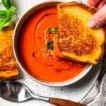 A hand dipping one half of a grilled cheese into a bowl of tomato soup. Recipe by Diethood.