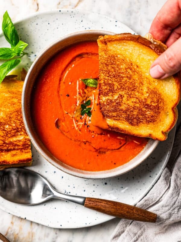 A hand dipping one half of a grilled cheese into a bowl of tomato soup. Recipe by Diethood.