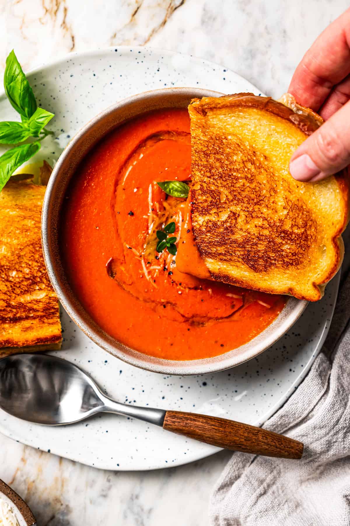 A hand dipping one half of a grilled cheese into a bowl of tomato soup. Recipe by Diethood.