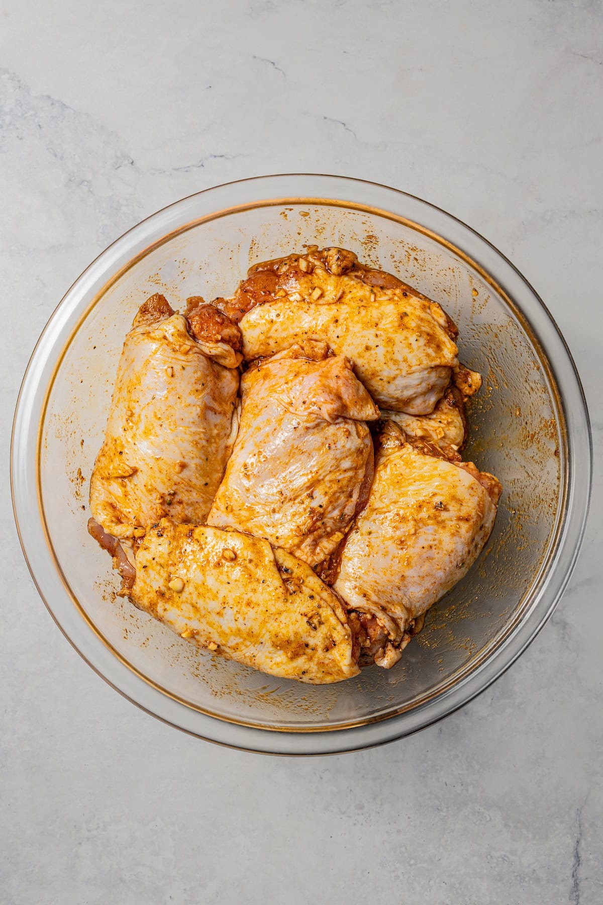 This homemade halal cart chicken over rice combines savory spice-rubbed chicken and fluffy rice, drizzled with the famous creamy white sauce! Chicken rubbed with spices in a glass bowl.