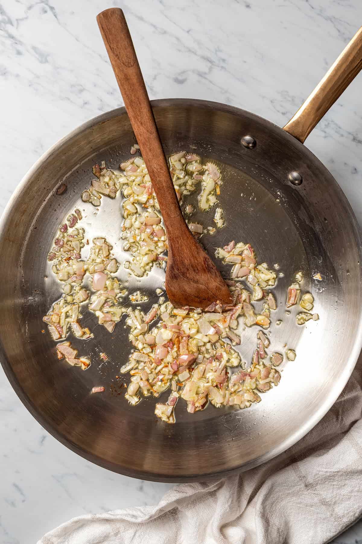 This stuffed chicken breasts recipe has a zesty Italian-inspired filling of fresh zucchini, tomatoes, and creamy cheeses, baked to perfection! Sautéed onions in a skillet with a wooden spatula.