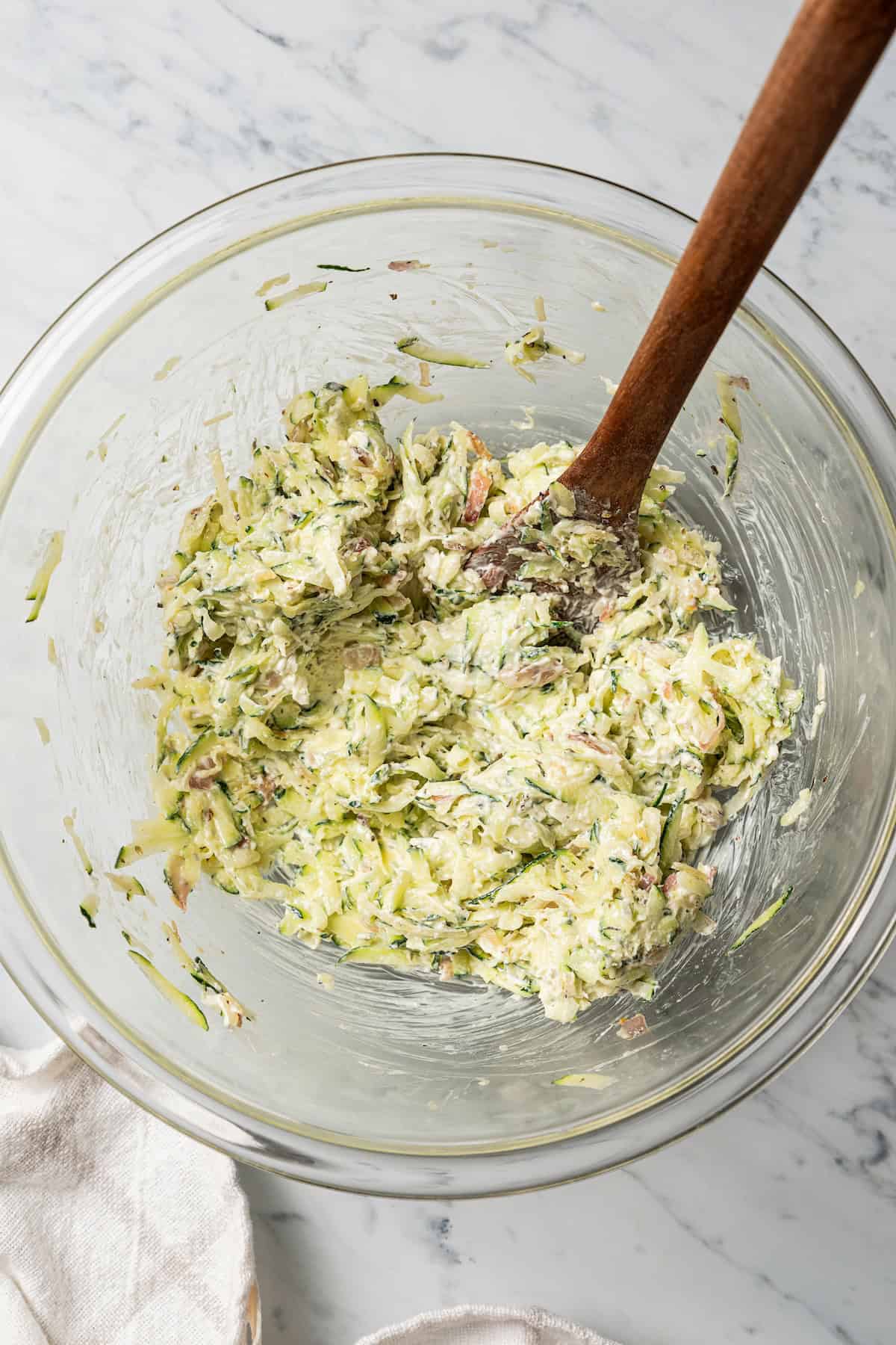 This stuffed chicken breasts recipe has a zesty Italian-inspired filling of fresh zucchini, tomatoes, and creamy cheeses, baked to perfection! Zucchini filling in a bowl with a wooden spatula.