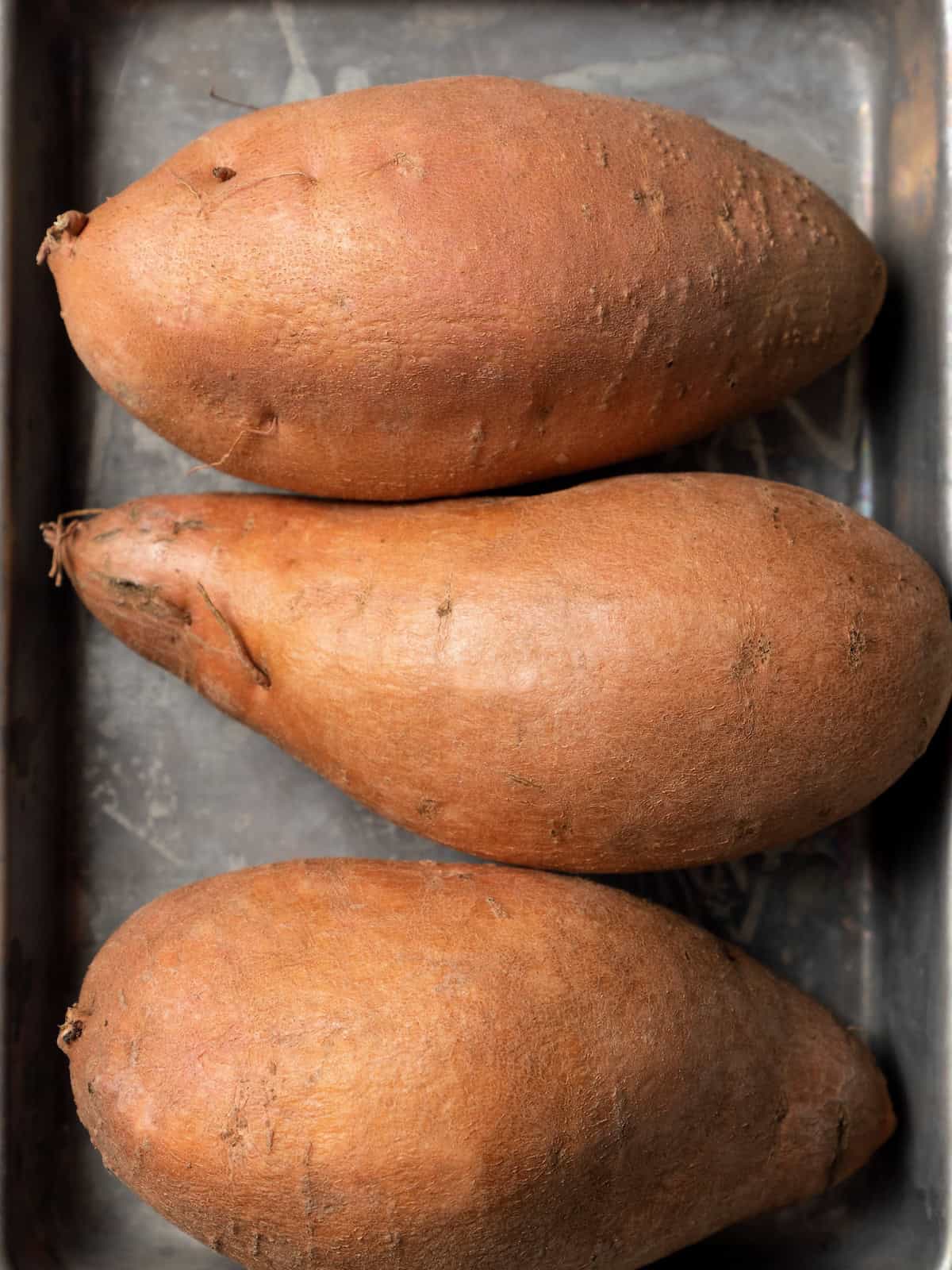 Close up of three large sweet potatoes on a baking sheet.