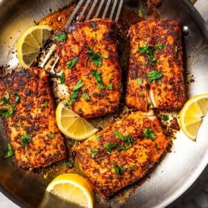 Mahi mahi in a skillet garnished with fresh herbs and lemon wedges. Photo by diethood.com