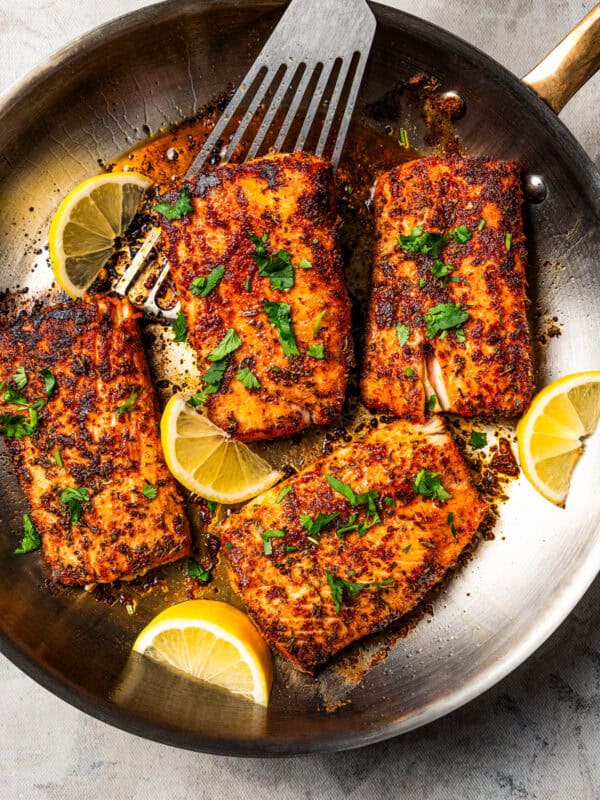Mahi mahi in a skillet garnished with fresh herbs and lemon wedges. Photo by diethood.com