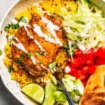 Chicken over rice in a bowl with flatbread, tomatoes, shredded salad, and a sour cream drizzle.