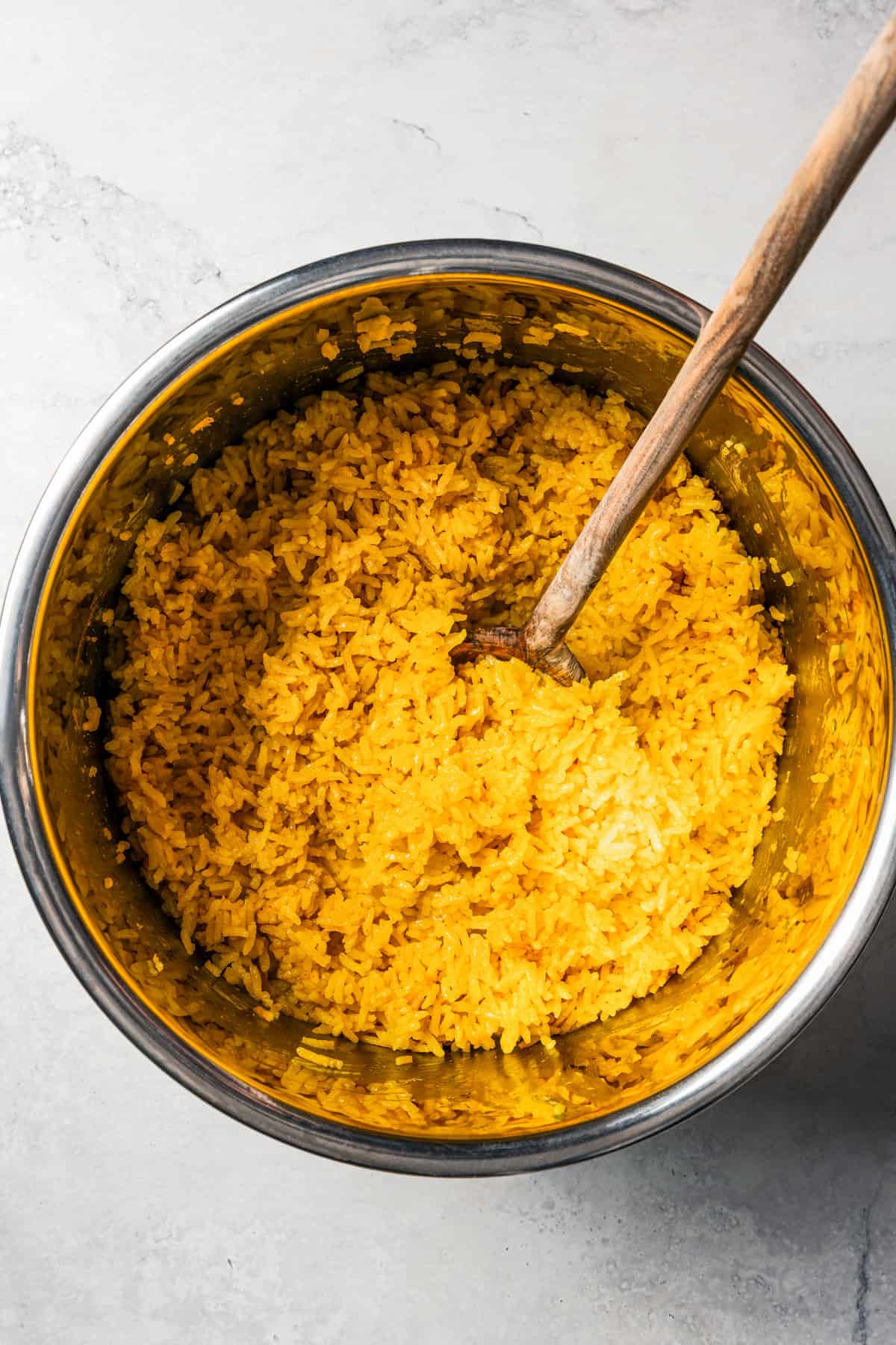This homemade halal cart chicken over rice combines savory spice-rubbed chicken and fluffy rice, drizzled with the famous creamy white sauce! Mixing through a large bowl of rice with a wooden spoon.