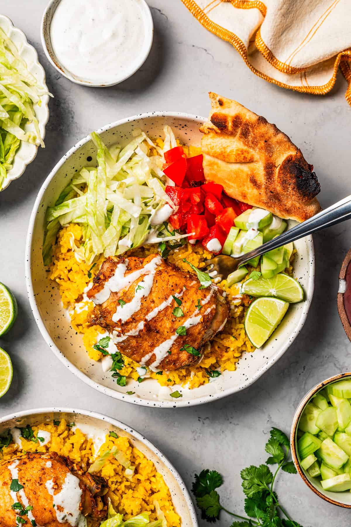 This homemade halal cart chicken over rice combines savory spice-rubbed chicken and fluffy rice, drizzled with the famous creamy white sauce! Overhead view of halal cart chicken over rice in a bowl with flatbread, garnishes, and a sour cream drizzle.