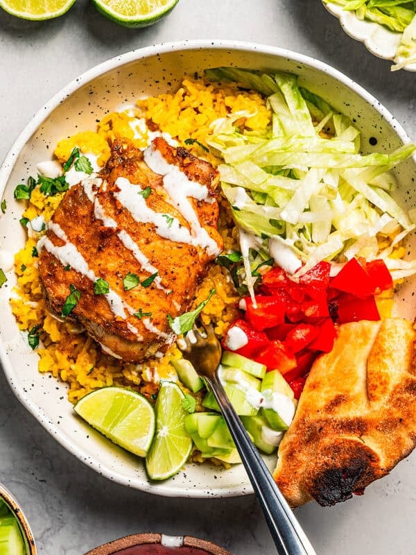 Halal cart chicken over rice in a bowl with flatbread, garnishes, and a sour cream drizzle.