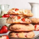 Four strawberry cheesecake cookies stacked on a plate with a bite missing from the top two cookies.