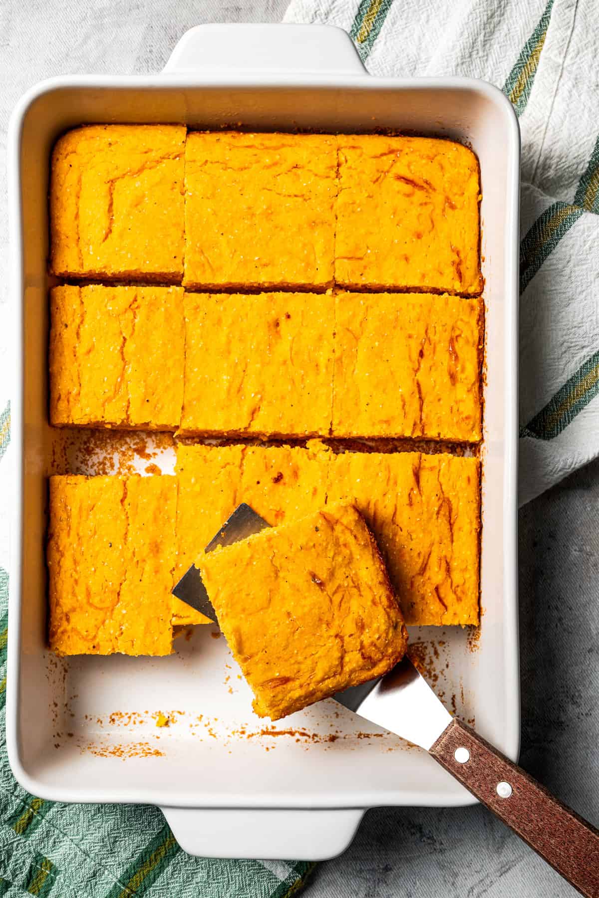 Overhead view of sweet potato cornbread slices in a casserole dish, with a spatula lifting one slice from the pan.