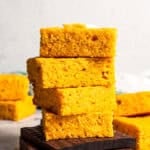 Four slices of sweet potato cornbread stacked, topped with a pat of butter.