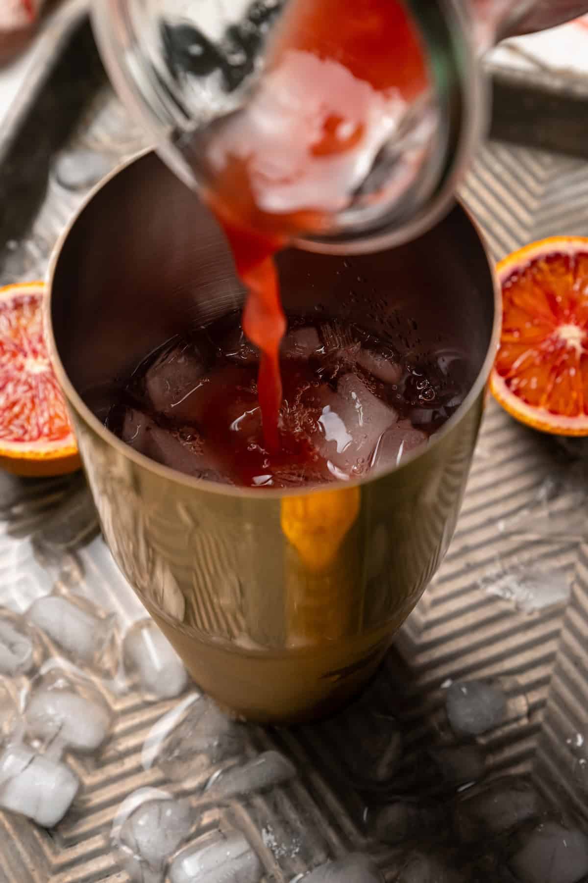 Blood orange juice being poured into a cocktail shaker with ice and the other margarita ingredients.