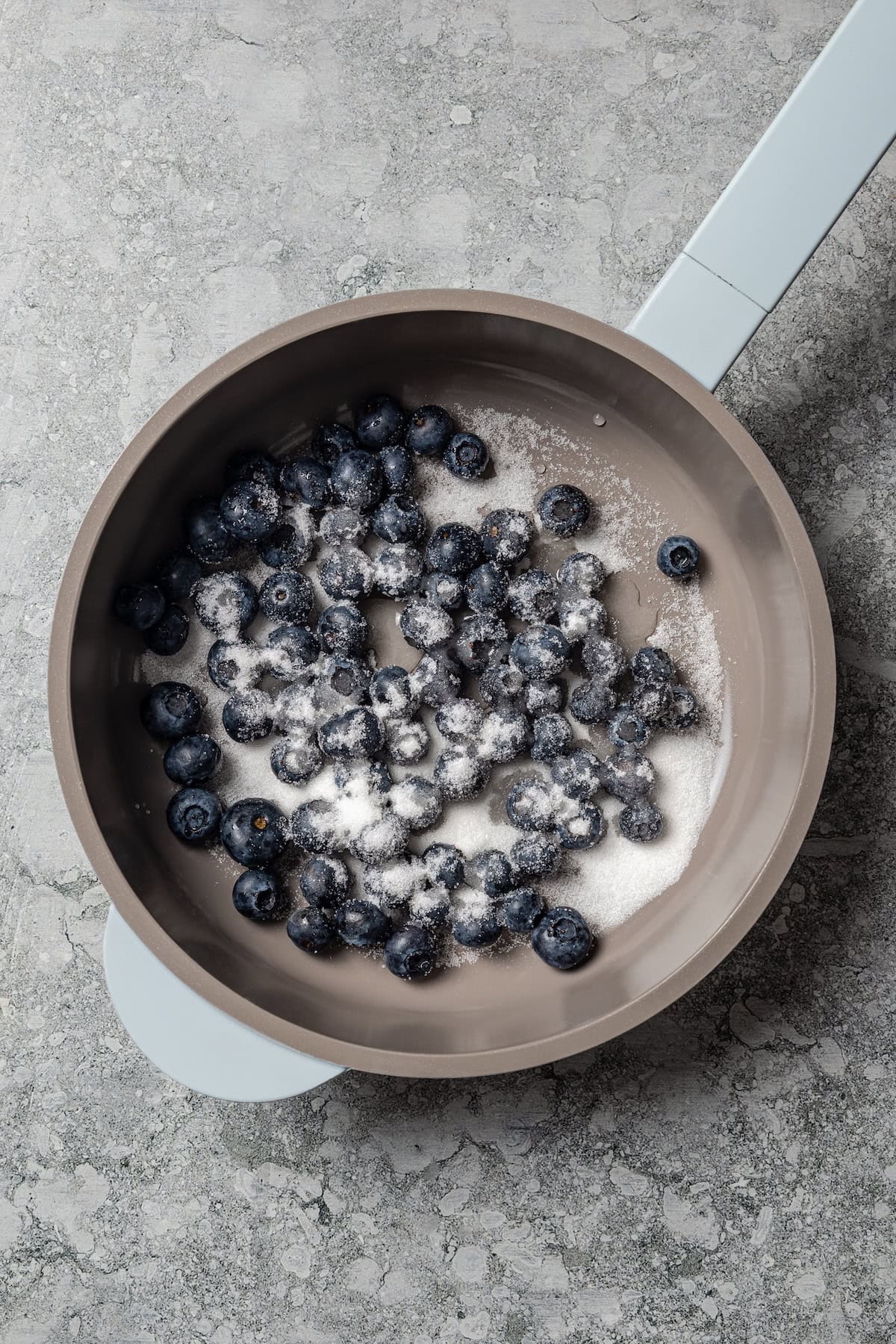 Blueberries combined with sugar in a saucepan.