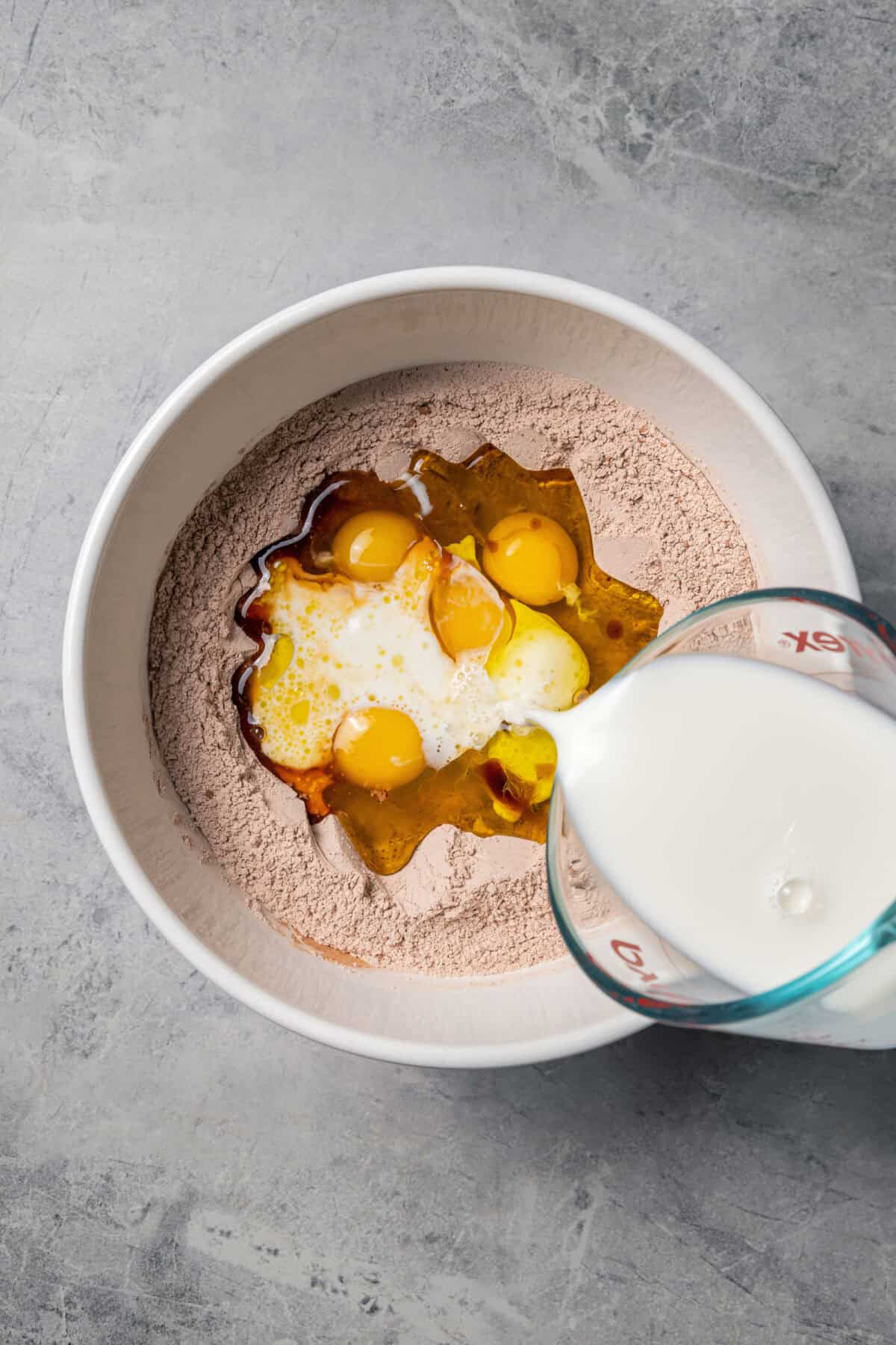 Pouring milk into a bowl of chocolate pancake ingredients.