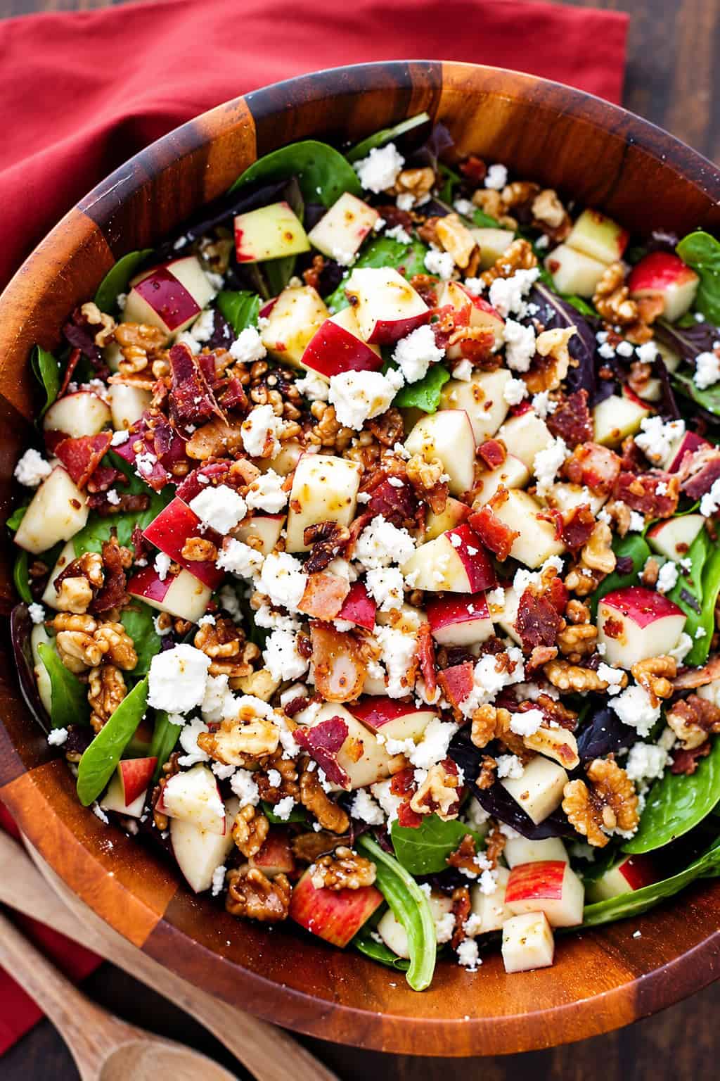 This apple salad recipe combines crisp fall apples tossed with smoky bacon, crunchy walnuts, and creamy feta in a sweet-tangy maple dressing. Apple bacon salad with mixed greens, chopped apples, bacon, feta cheese, and nuts in a wooden bowl.