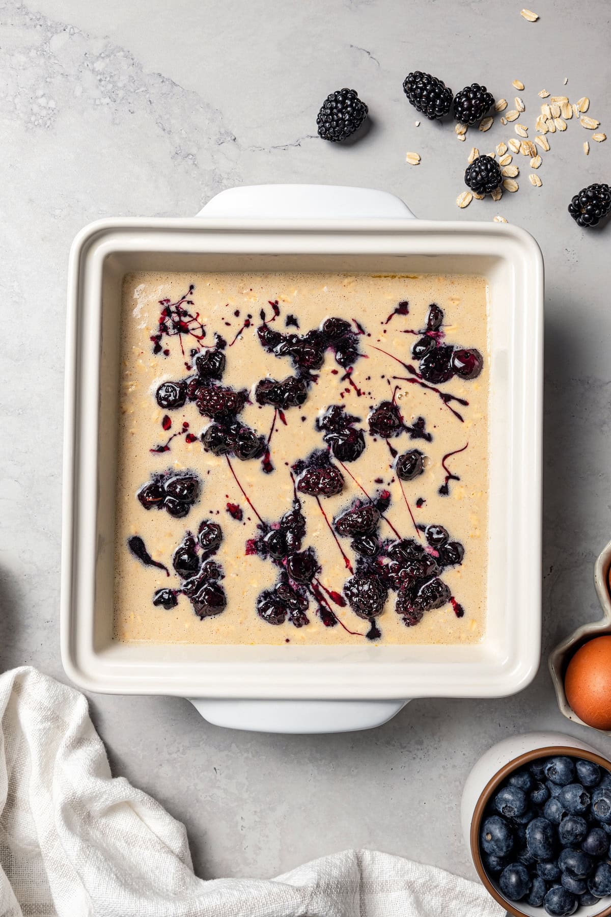 This baked oatmeal is loaded with protein from wholesome oats, almond butter, eggs, and protein powder. It's delicious, swirled with a juicy berry compote. Overhead view of protein baked oatmeal batter swirled with berry compote in a baking dish.