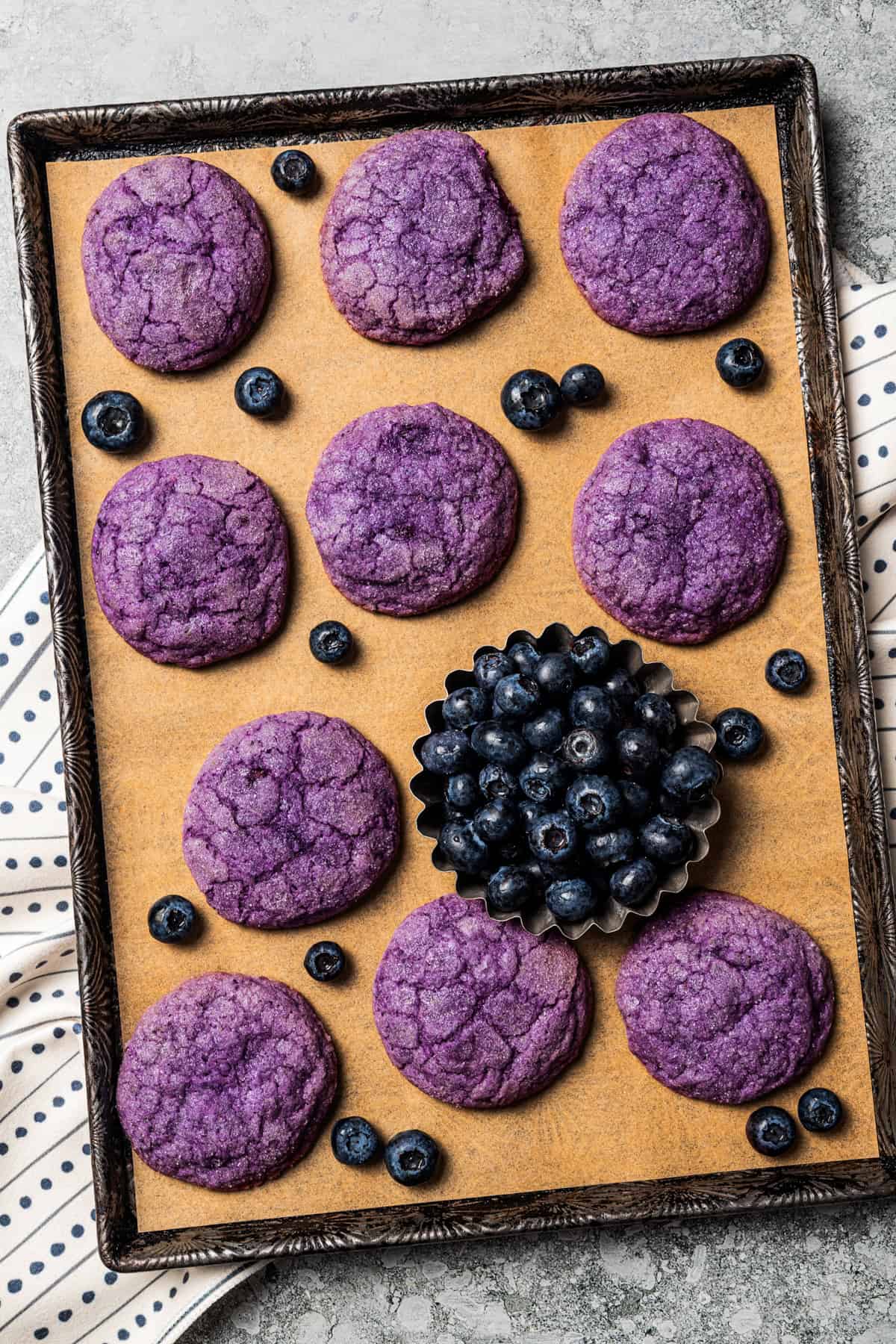 Blueberry cookies on a lined baking sheet with a bowl of fresh blueberries set next to the cookies.