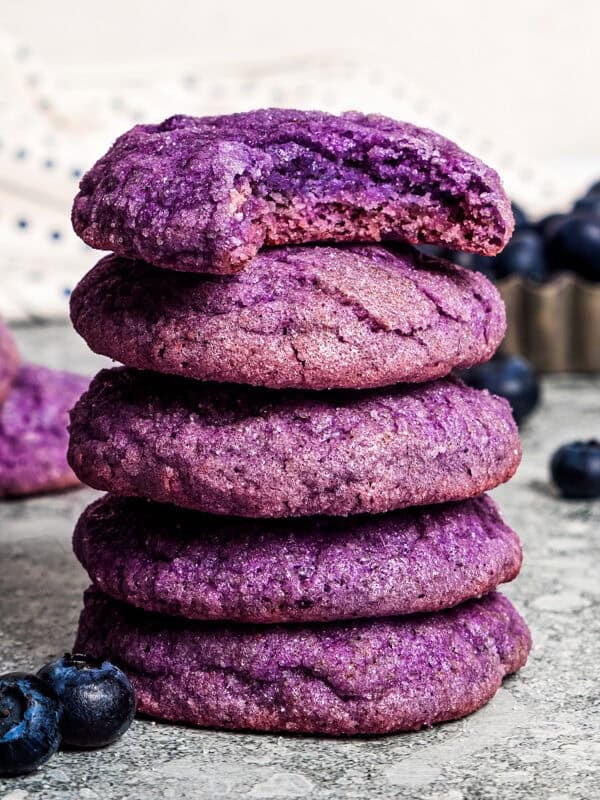 A stack of blueberry cookies on a countertop with a bite missing from the top cookie.