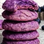 A stack of blueberry cookies on a countertop with a bite missing from the top cookie.