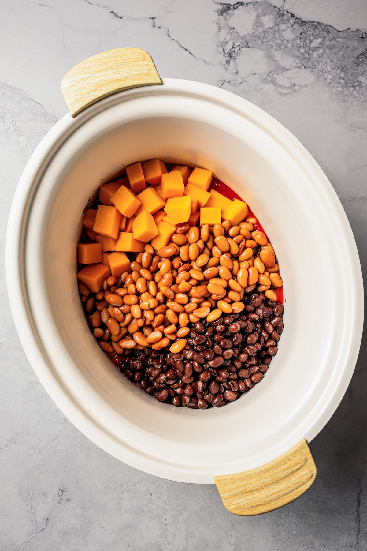 Diced butternut squash and chili ingredients are combined inside the slow cooker.