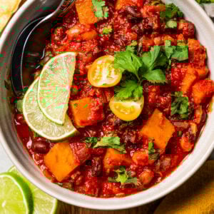A bowl of butternut squash chili garnished with lime wedges.