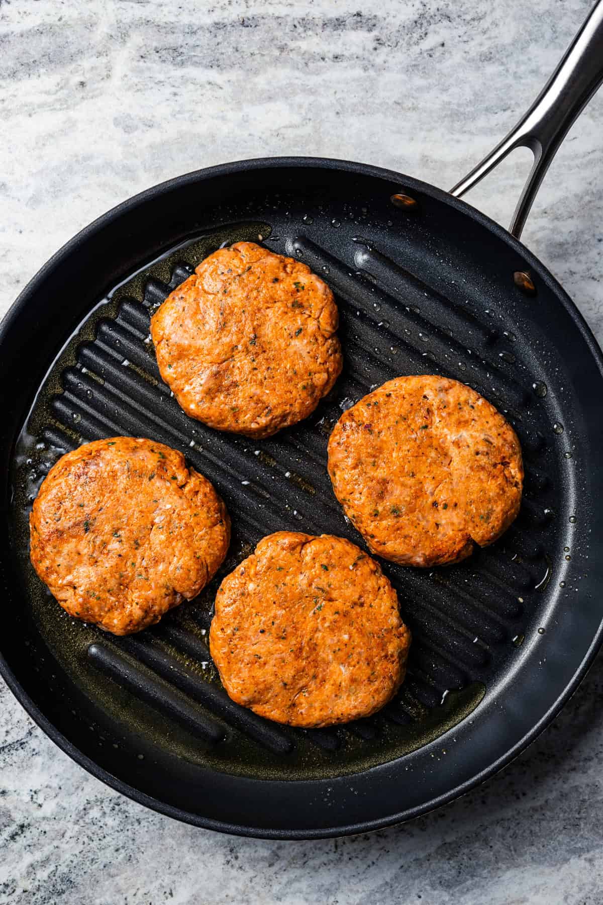 Four chicken burger patties in a cast iron skillet.