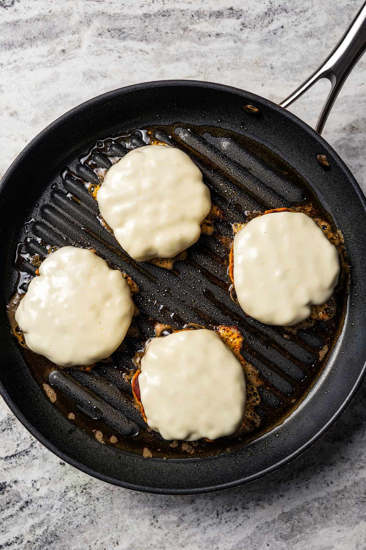 A skillet with four burger patties topped with cheese.