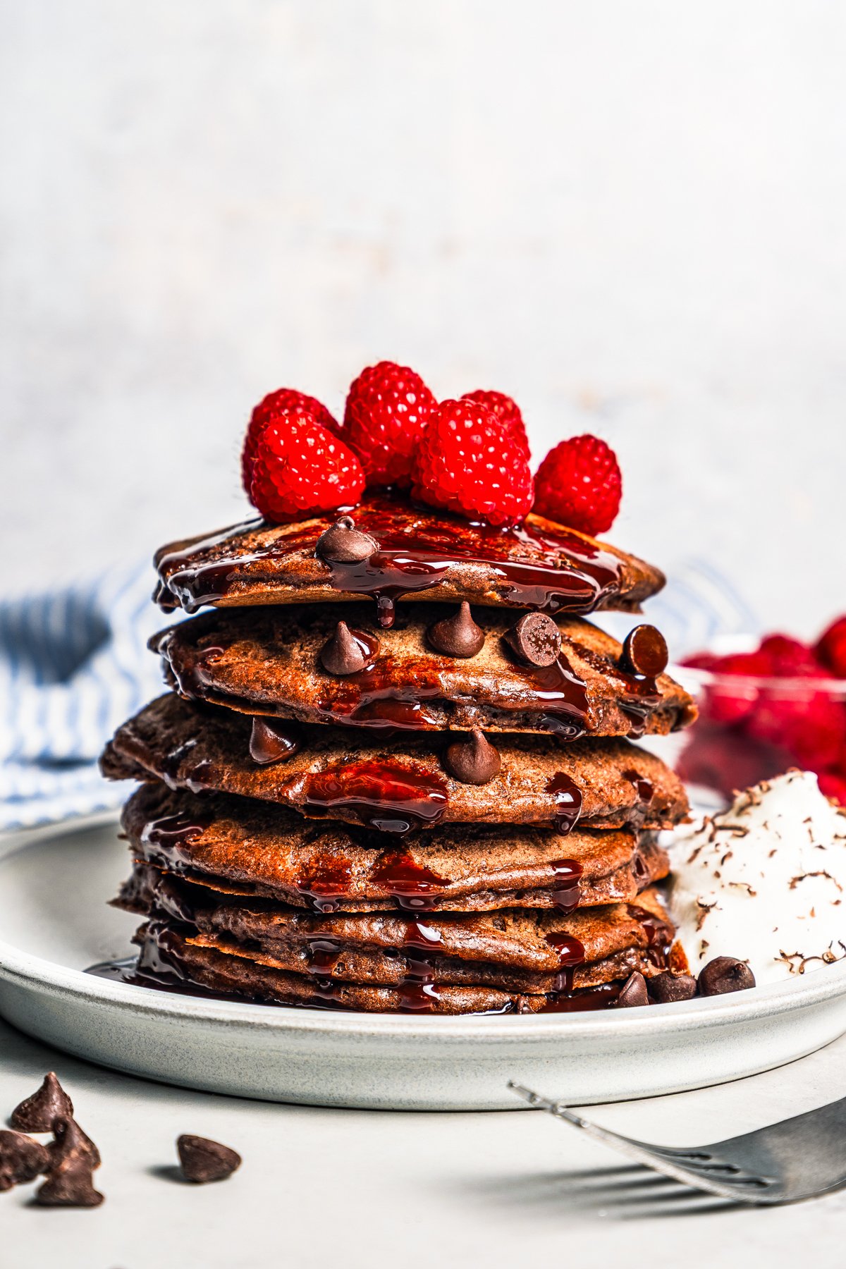 Chocolate pancakes topped with chocolate sauce and raspberries on a plate.