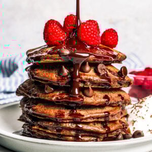 Pouring chocolate sauce over a stack of pancakes.