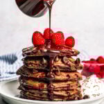 Pouring chocolate sauce over a stack of pancakes.