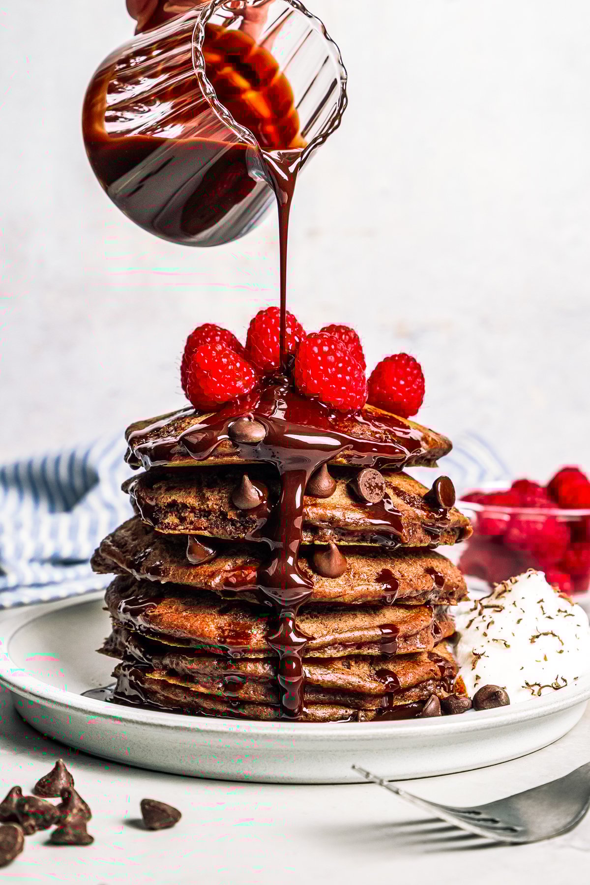 Pouring chocolate sauce over a stack of pancakes.