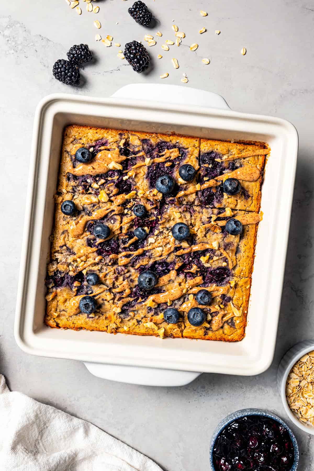 This baked oatmeal is loaded with protein from wholesome oats, almond butter, eggs, and protein powder. It's delicious, swirled with a juicy berry compote. Baked oatmeal in white a baking dish.