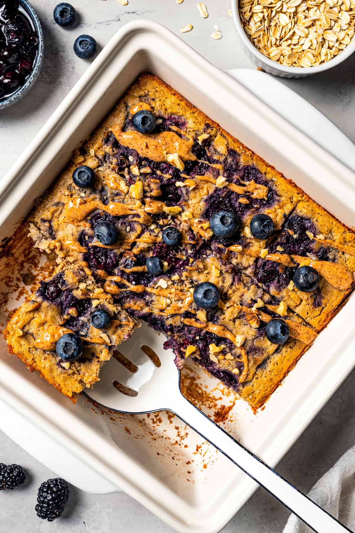 This baked oatmeal is loaded with protein from wholesome oats, almond butter, eggs, and protein powder. It's delicious, swirled with a juicy berry compote. A spatula tucked underneath a slice of protein baked oatmeal next to the rest of the baked oatmeal in a baking dish. Photo by diethood.