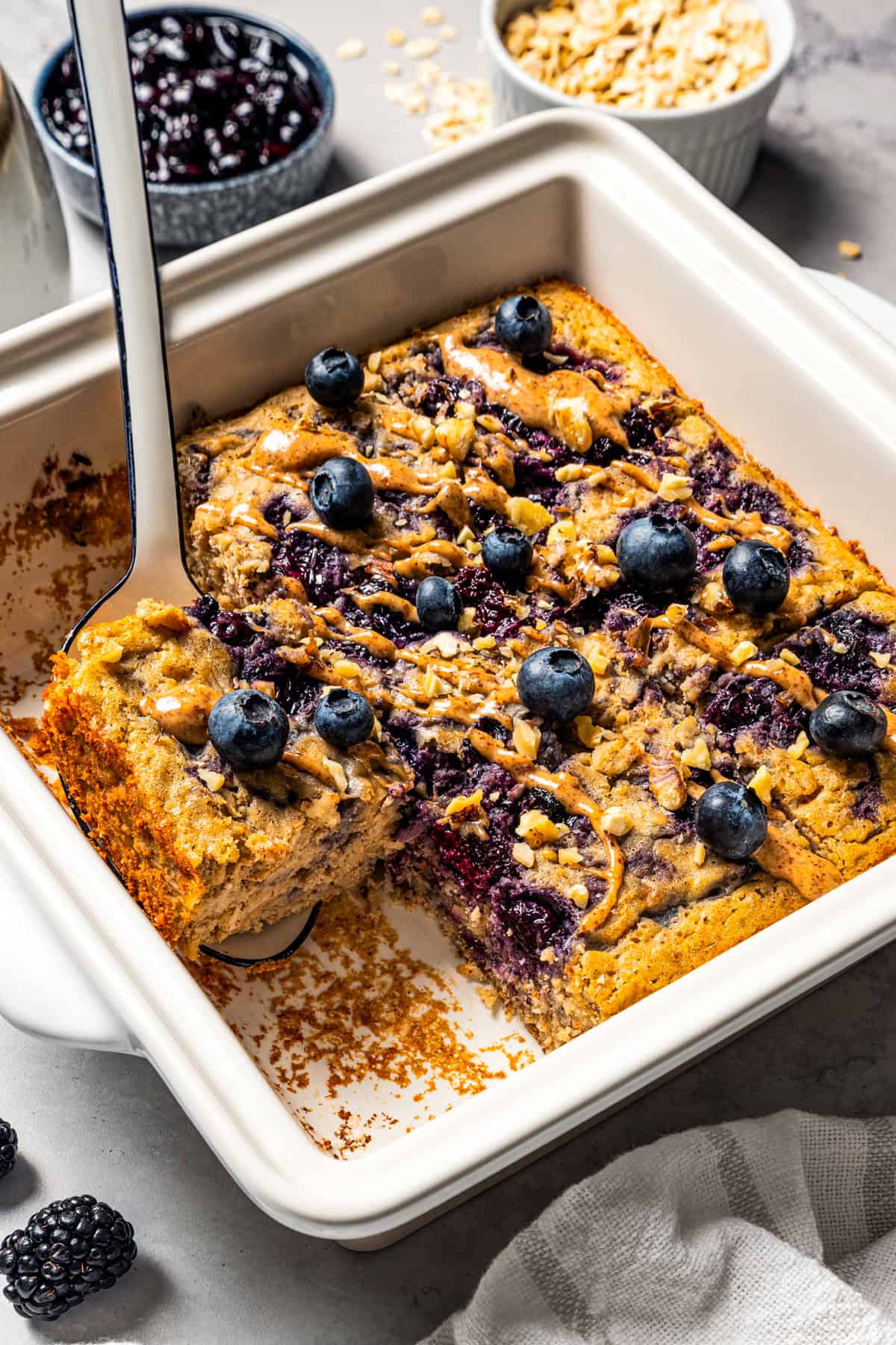 This baked oatmeal is loaded with protein from wholesome oats, almond butter, eggs, and protein powder. It's delicious, swirled with a juicy berry compote. A spatula tucked underneath a slice of baked oatmeal next to the rest of the baked oatmeal in a baking dish.