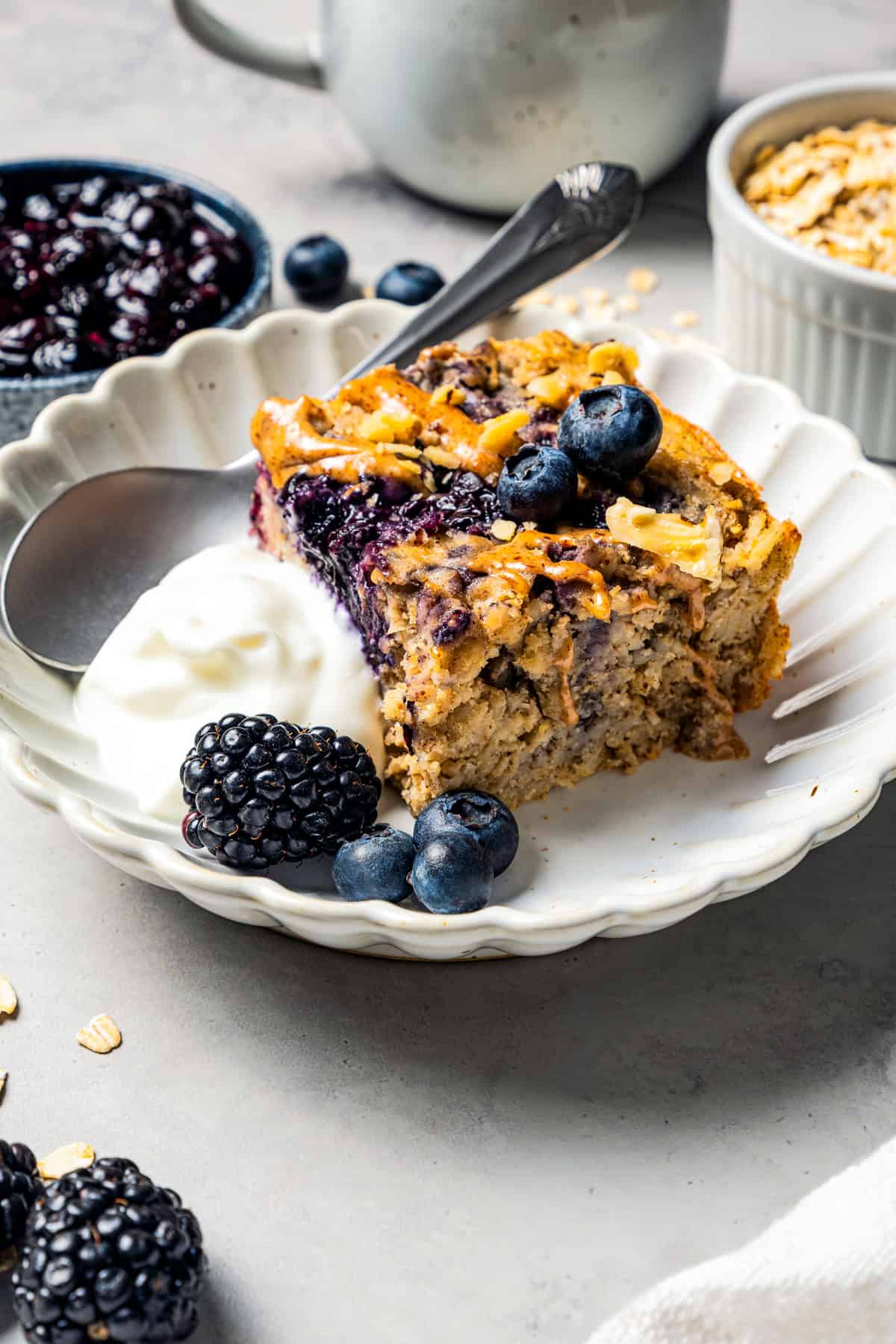 This baked oatmeal is loaded with protein from wholesome oats, almond butter, eggs, and protein powder. It's delicious, swirled with a juicy berry compote. A slice of protein baked oatmeal on a plate with a side of yogurt and a garnish of fresh berries.
