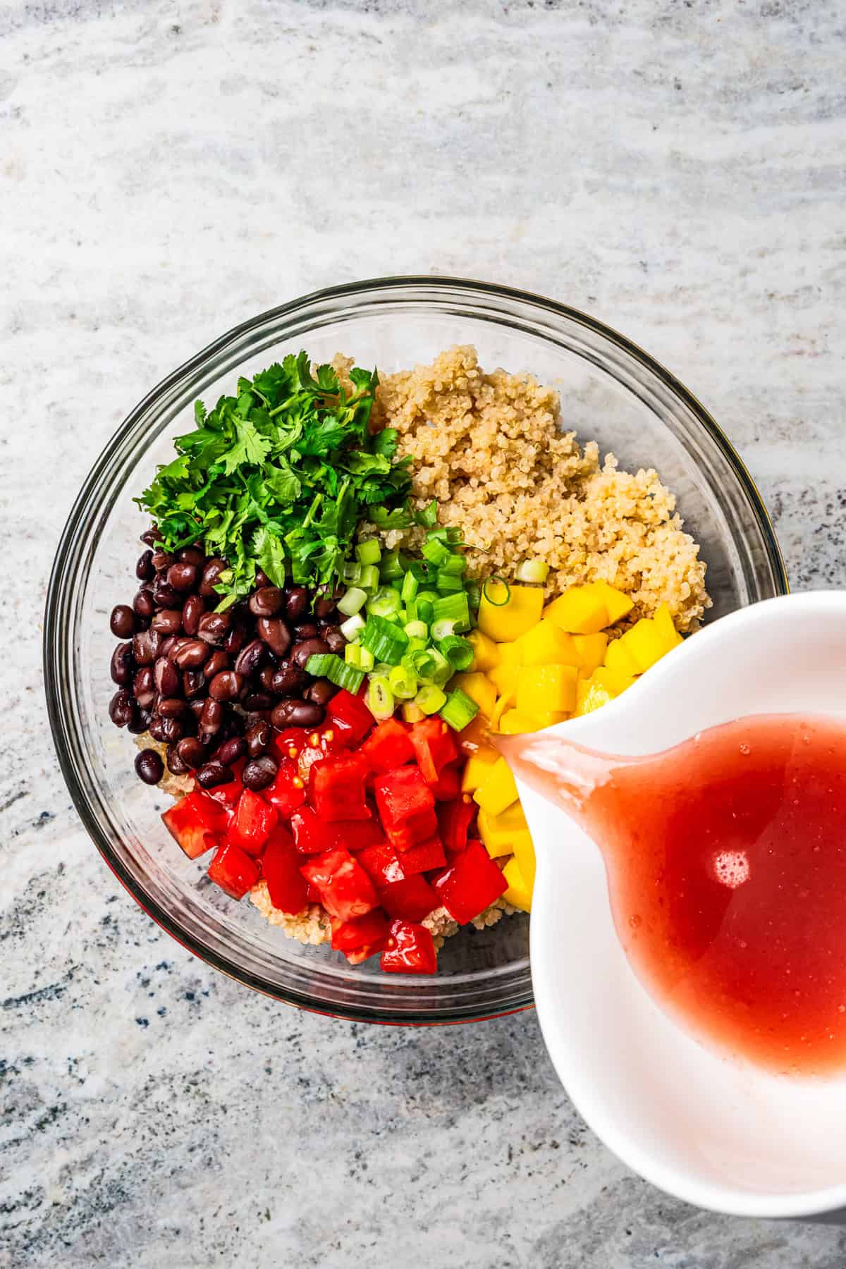 Dressing being poured over quinoa salad ingredients in a bowl.