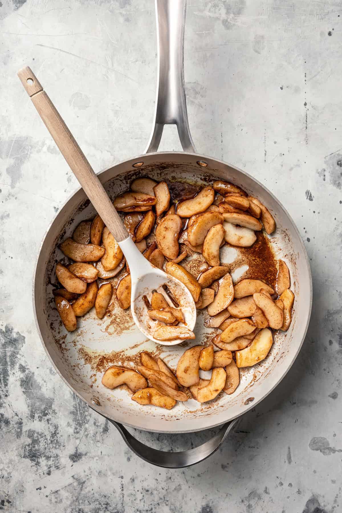 Cinnamon apples in a skillet with a spoon.