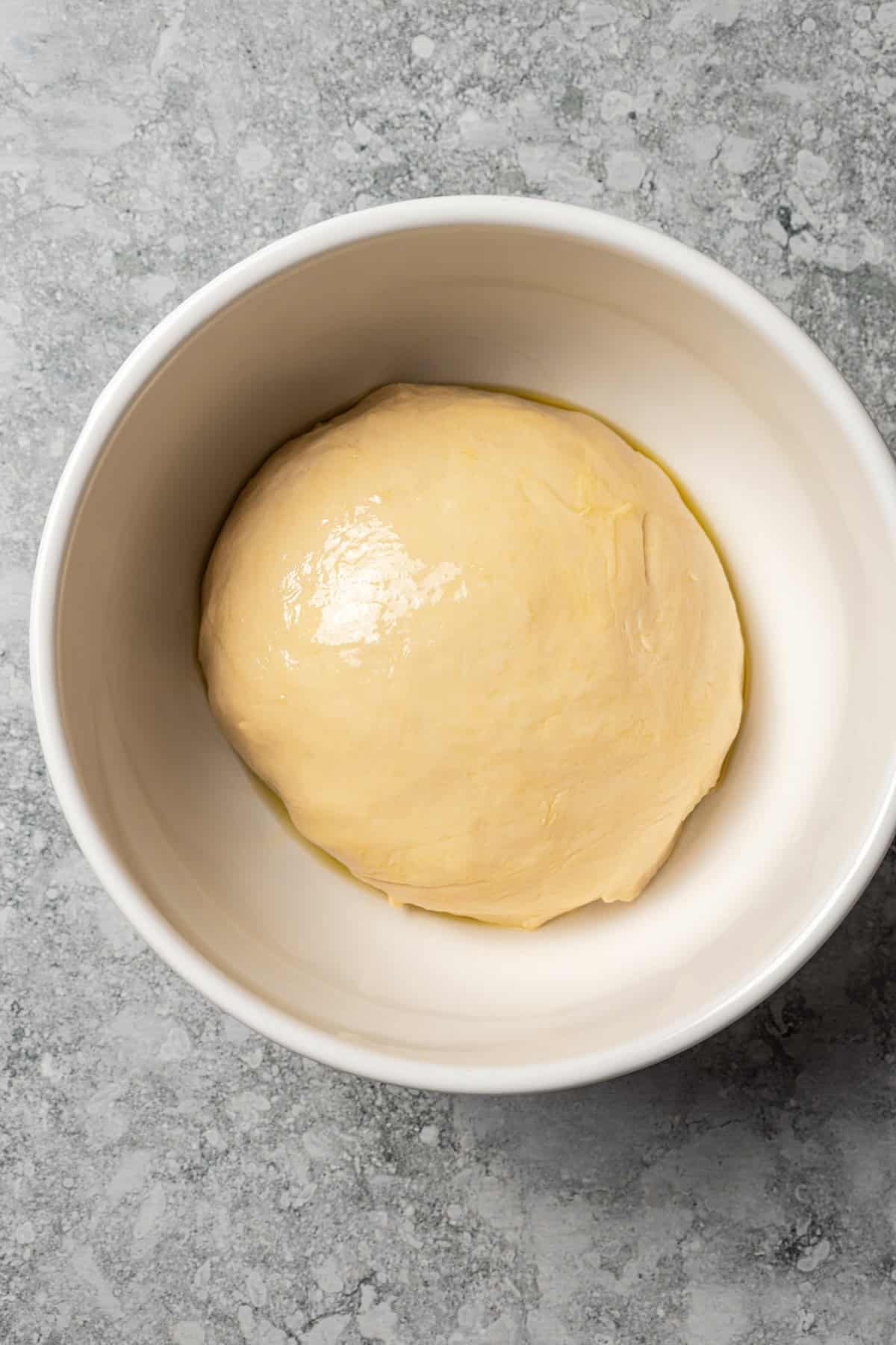 Overhead view of a ball of cinnamon roll dough in a bowl.