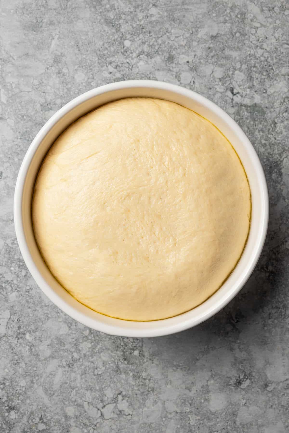 Overhead view of a risen ball of cinnamon roll dough in a mixing bowl.