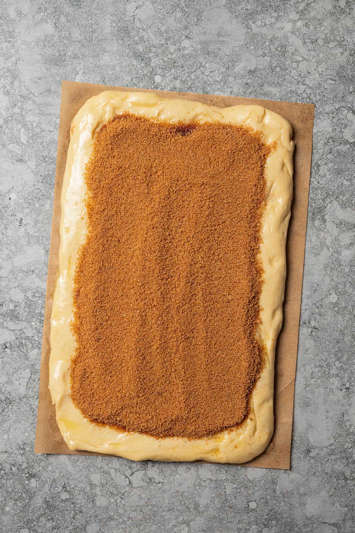 Overhead view of cinnamon sugar filling spread over a rolled out rectangle of dough on a countertop.