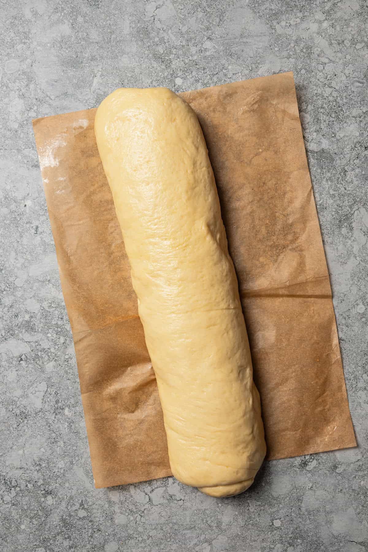 Overhead view of a rolled up log of cinnamon roll dough on a sheet of parchment paper on a countertop.