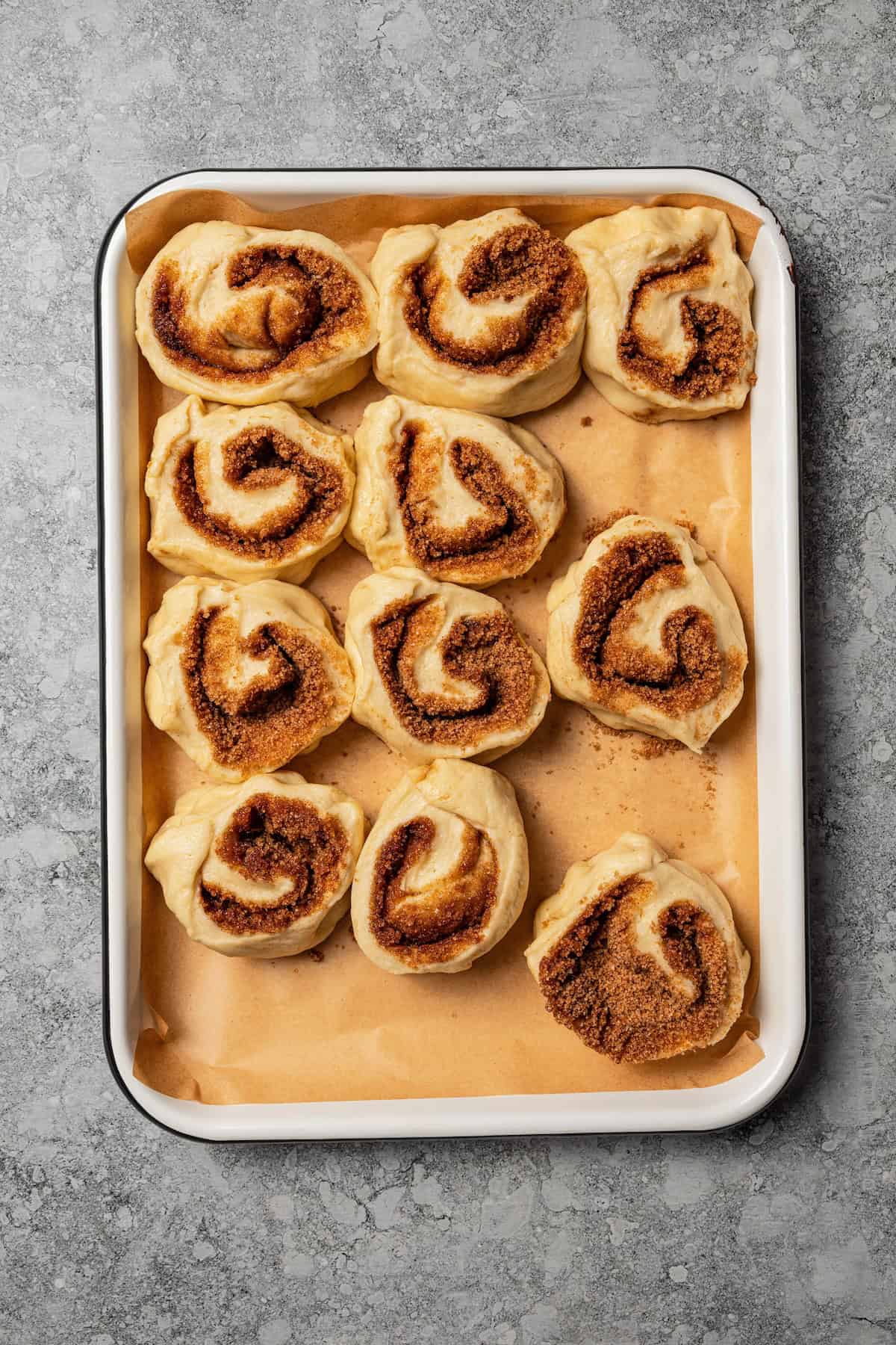Overhead view of cut cinnamon rolls on a lined baking sheet.